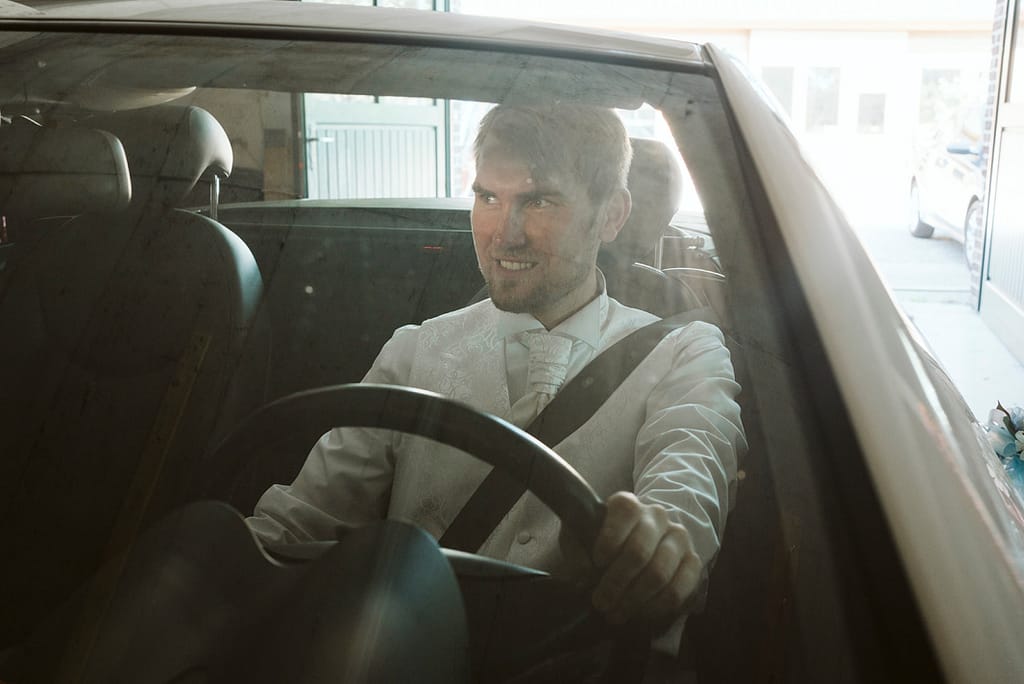 Bräutigam hinterm Steuer eines Cabriolets beim Rückwärtsrausfahren.