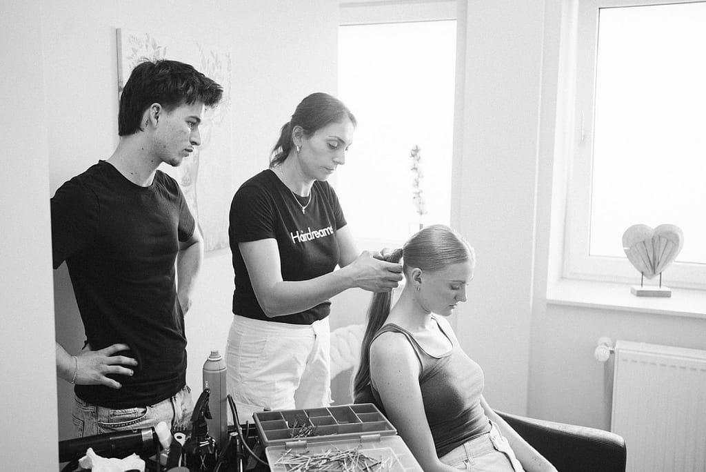 Das Friseurteam bei der Arbeit am Styling der Braut. Bild in Schwarzweiß.