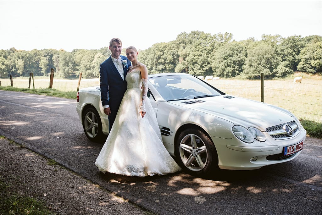 Das Hochzeitspaar vor einem weißen Cabriolet.