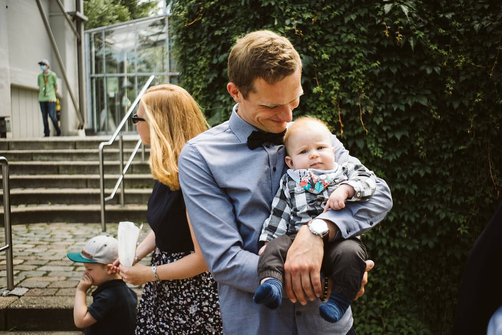 Ein Vater mit seinem Kind auf dem Arm. Er blickt zu idem Kind. Das Kind ist sehr jung und blickt in die Kamera.