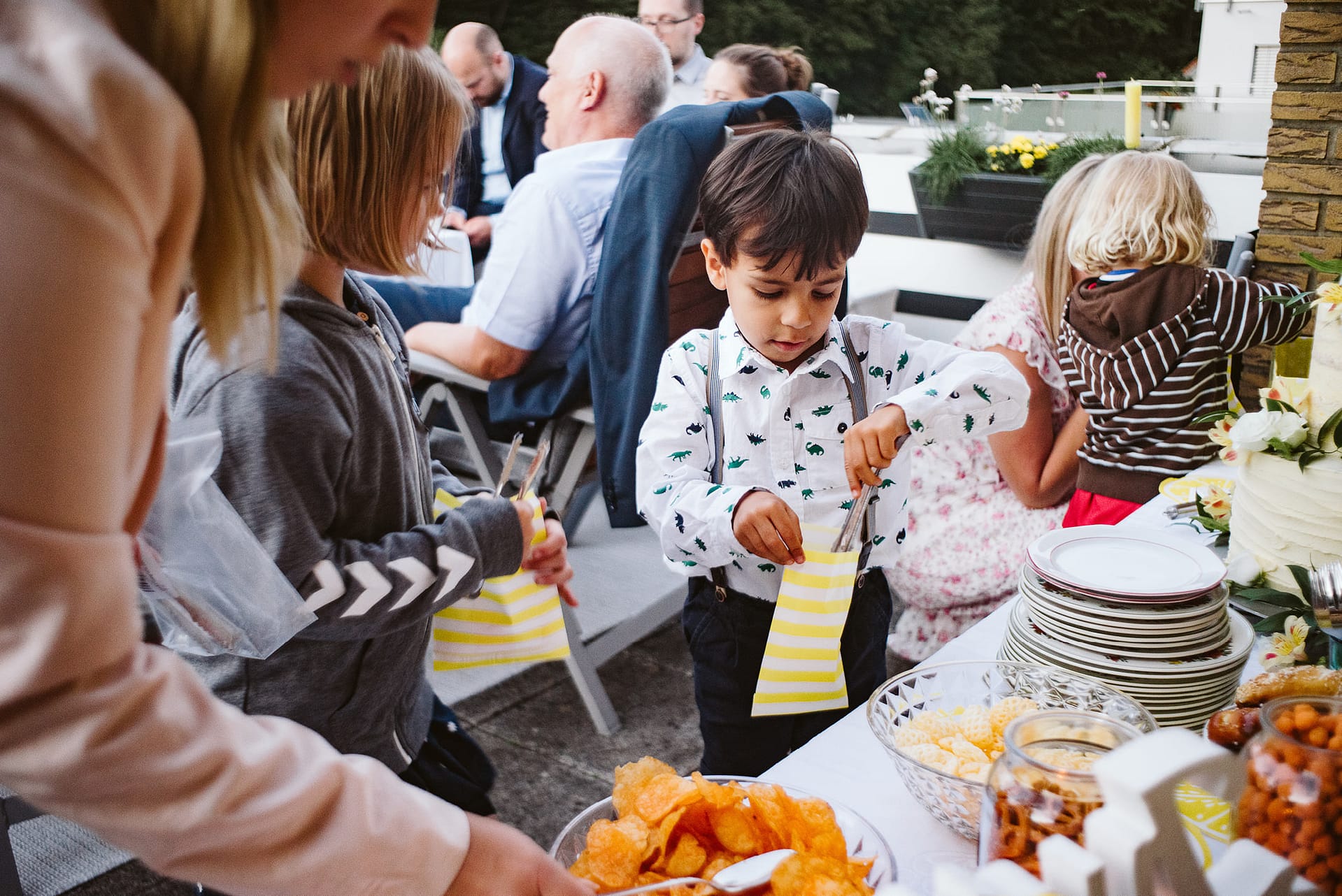 Ein kleiner Junge bedient sich am Süßigkeitenbuffet. im Hintergrund sind andere Kinder und Gäste zu sehen.