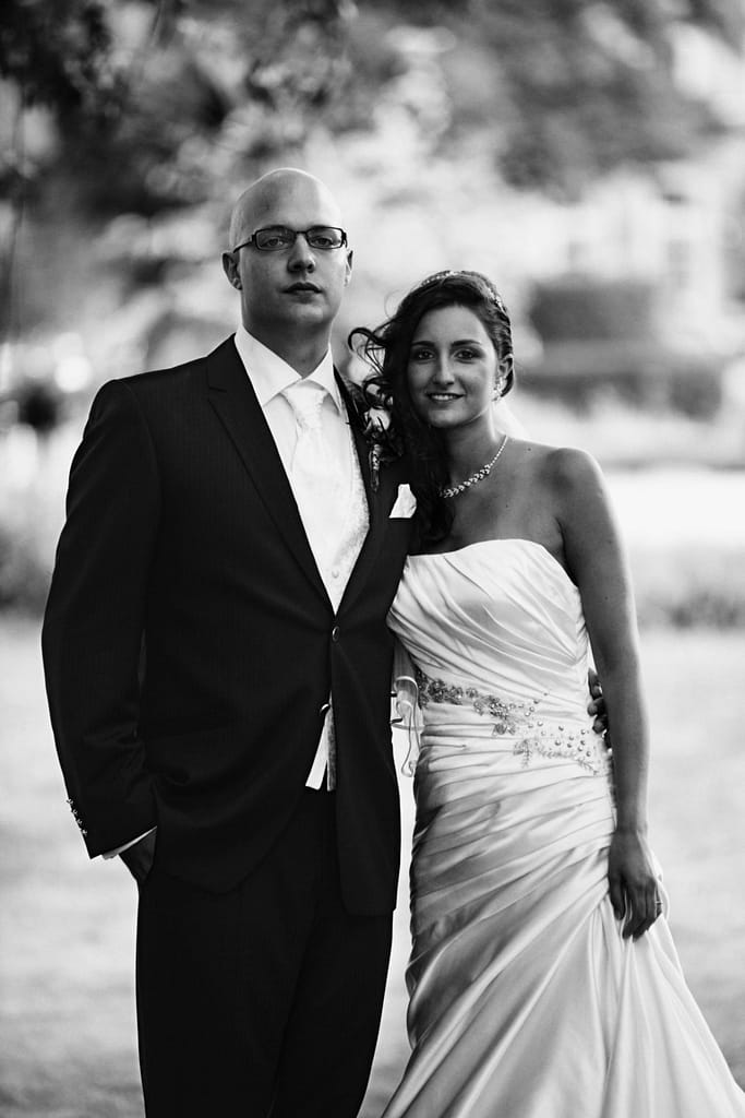 Schwarzweiß-Portrait von Sabrina und Tobias im Hochzeitsoutfit vor unscharfem Hintergrund