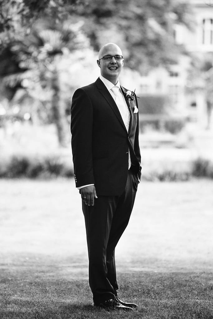 Portrait von Tobias im Hochzeitsanzug vor unscharfem Parkhintergrund