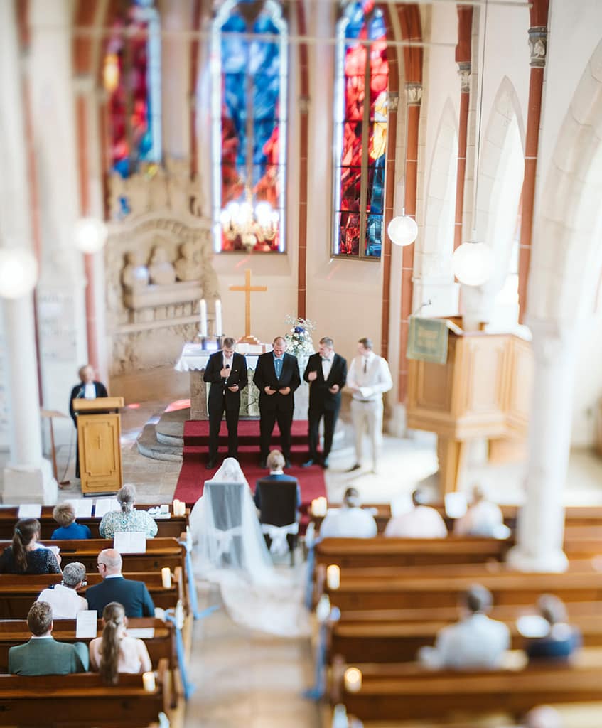Vorderer Teil des Kirchenschiffes von oben, während vier Menschen vor dem Brautpaar Fürbitten halten.